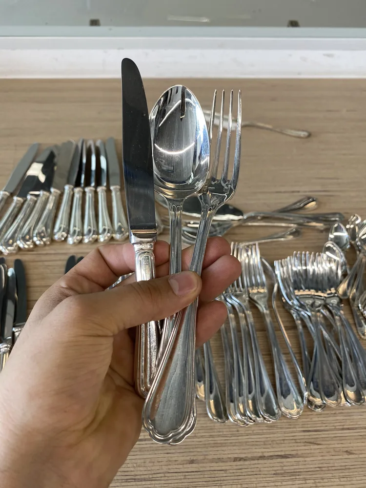 Poignée de couverts en argent tenue en main devant une ménagère sortie de son coffret