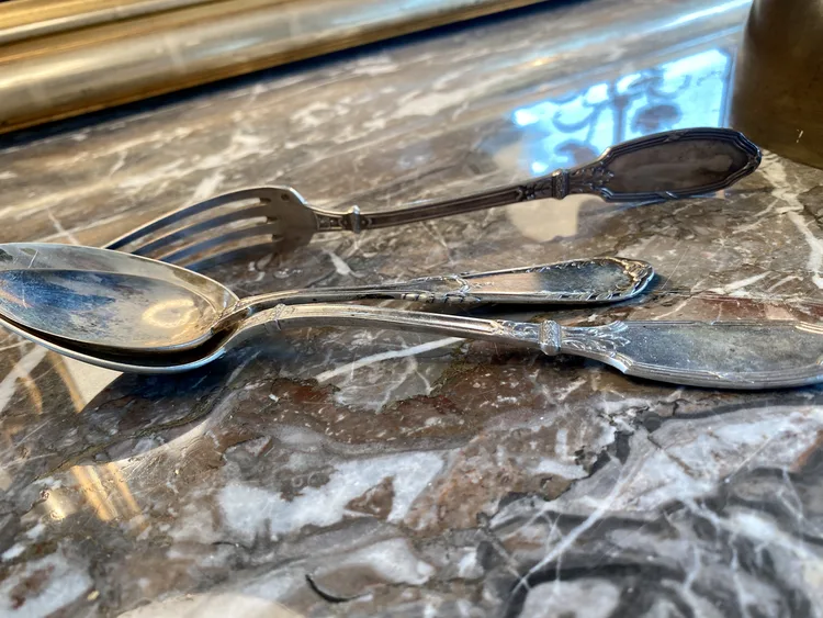 Fourchette et deux cuillères en argent de modèles différents posées sur un plateau de marbre